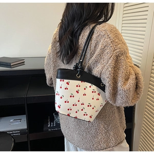 Detailed side view of a white bucket bag with red cherry prints and black knotted handles