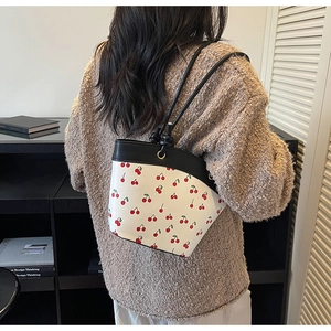 Detail view of the white cherry print bucket bag styled with a warm knit sweater