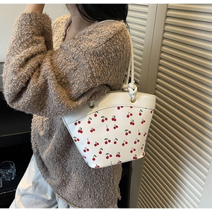 Detail of white PU leather bucket bag featuring red cherry prints and woven handles