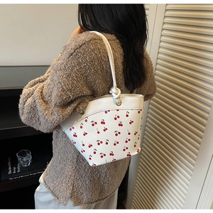 Detail view of white bucket bag with cherry print and knotted rope shoulder strap