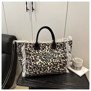 Close-up of leopard print tote bag featuring white fringe tassels and sturdy black handles