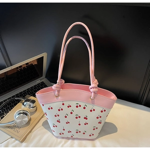 Pink and white cherry print tote bag with knotted cord handle shown in a lifestyle desk setting