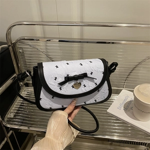 Bow knot crossbody bag with heart pendant and contrast piping shown in a lifestyle setting