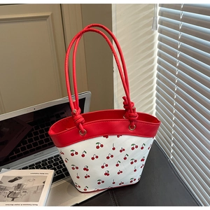 Close-up of stylish cherry print tote bag with red leather straps in a home office setting
