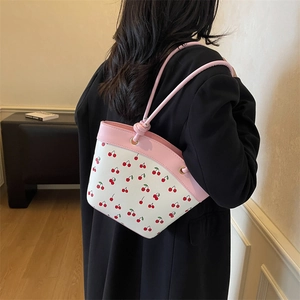 Chic pink and white bucket bag with cherry print shown on model in a cozy indoor setting