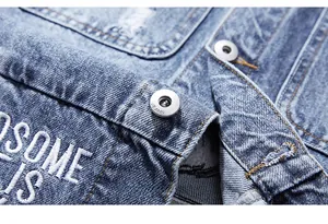 Détail du gilet en jean bleu avec broderie blanche en bouclette et boutons métalliques