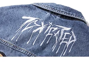 Détail de la broderie graffiti blanche au dos d'un gilet en jean bleu pour homme