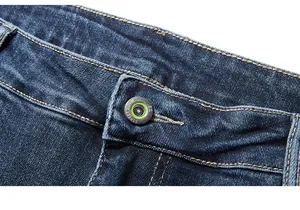 Detail of metal button with green ring and stitching on dark blue denim jeans