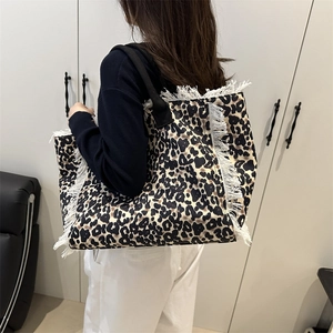 Large leopard print tote bag with frayed edges and wide black shoulder strap on model