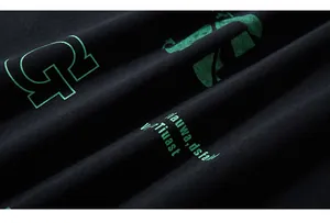 Close-up of bright green screen-printed letters on black knit fabric of oversized hoodie