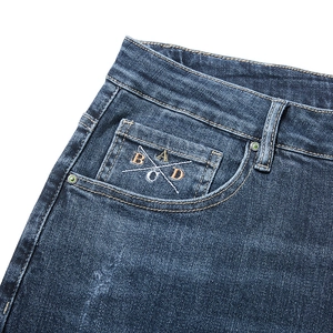 Macro shot of dark blue denim jeans featuring unique cross-line letter embroidery on pocket