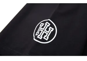 Vue détaillée du logo H géométrique blanc imprimé sur le tissu en coton noir du t-shirt
