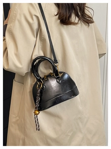 Detail of black glossy shell bag with gold hardware and woven charm on trench coat