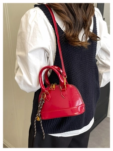 Macro detail of red shell-shaped handbag showing glossy texture and rope charm detail