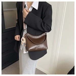 Detail van bruine leren emmer tas met geometrische band en pluchen hanger sieraad