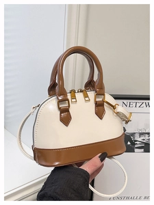 Close-up of cream white shell bag with brown trim, dual zippers and gold hardware