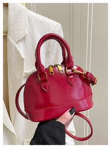 Detail of red patent leather shell bag with gold zippers and adjustable shoulder strap