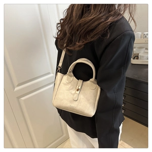 Detail view of cream bucket bag with metal lock and FASHION logo on a female model