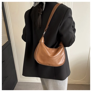 Close-up of brown crescent bag with FASHION & BAGS logo detail and leather texture