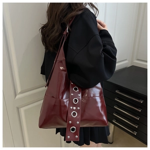 Détail du cabas en cuir verni rouge foncé avec œillets métalliques et rivets vintage