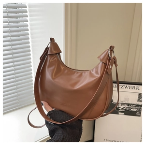 Detail of a brown leather crescent shoulder bag with silver zipper and metal rings