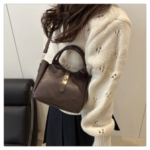 Detail of dark brown leather bucket bag with gold lock and textured lychee grain finish