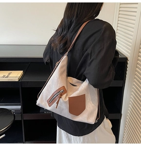 Detail of a large beige canvas tote bag with brown leather accents and a thin shoulder strap