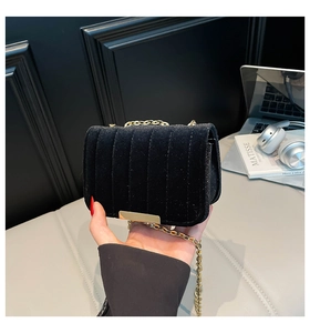 Close-up of black velvet crossbody bag featuring vertical stitching and golden chain strap