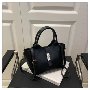 Detail of black trapezoid bucket bag with gold twist lock and adjustable shoulder strap