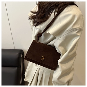 Detail of dark brown suede shoulder bag with gold clasp and knotted strap on beige coat