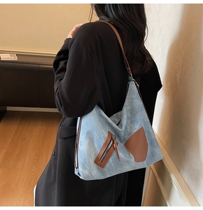 Detail of blue denim tote bag with brown leather straps and pockets worn by a model