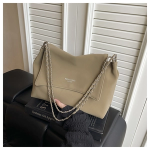 Close-up of khaki faux leather shoulder bag with silver chain straps on art books