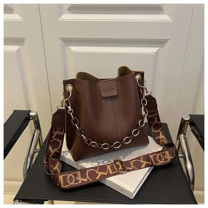Detail of dark brown lychee leather bucket bag with golden chain and jacquard strap