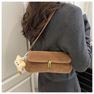 Close-up of brown suede underarm bag with gold twist lock and star charm on grey sweater