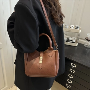 Brown leather bucket bag with gold buckle and crossbody strap shown on a model