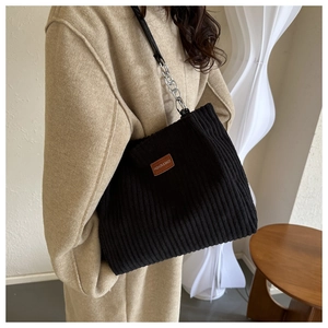 Detail of black corduroy tote bag featuring vertical texture and metal chain strap