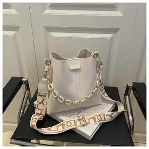 Detail of white bucket bag featuring litchi grain leather and artistic wide strap