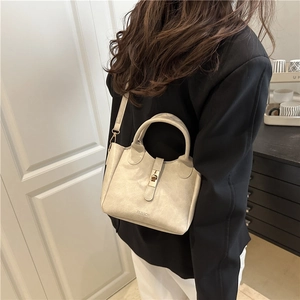 Minimalist cream leather bucket bag with top handle and gold clasp for crossbody wear