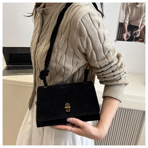 Detail of black suede shoulder bag with golden twist lock and thick woven strap