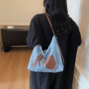 Blue canvas tote bag with brown leather straps shown on model in a minimalist setting