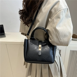 Fashionable black bucket bag with gold lock and adjustable strap worn with a trench coat