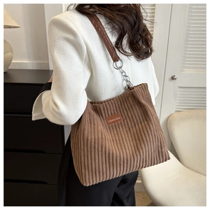 Close-up of brown corduroy tote bag featuring leather logo patch and metal chain strap