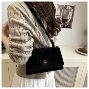 Close-up of black suede crossbody bag with gold metal buckle shown on a model