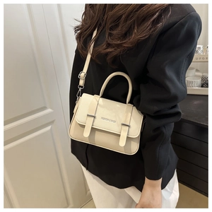Lifestyle shot of an off-white faux leather crossbody bag with top handle and strap