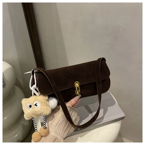 Detail view of brown suede shoulder bag with gold twist lock and furry monster pendant