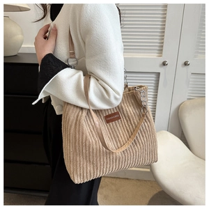 Detail of beige corduroy tote bag featuring a leather logo patch and metal chain strap