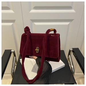 Detail view of the burgundy suede crossbody bag with gold lock and knotted shoulder strap