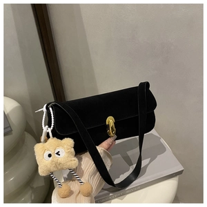 Detail of black matte underarm bag with gold clasp and yellow plush charm accessory