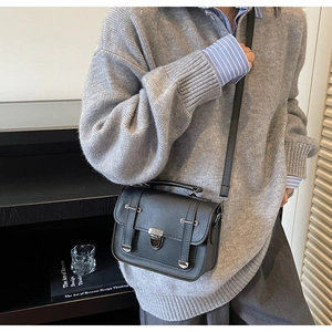 Side view of a vintage black leather crossbody bag worn with a casual grey knit outfit