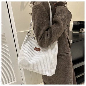 Close-up of white corduroy tote bag featuring silver chain straps and brown leather tag